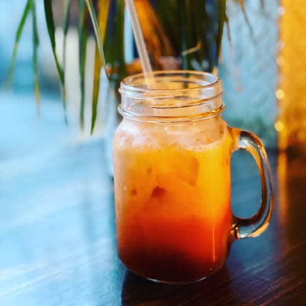 A mason jar of Noodle 501's Thai iced tea with a straw, on a wooden table.