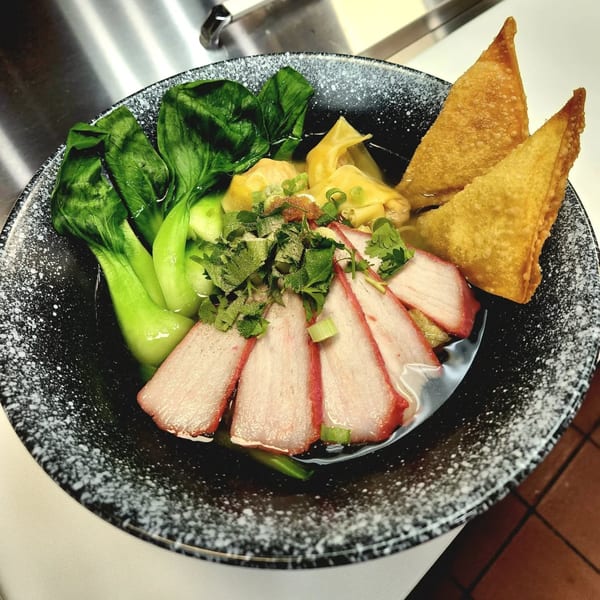 Noodle 501's wonton noodle soup with bok choy, sliced pork, and fried wontons in a black bowl.