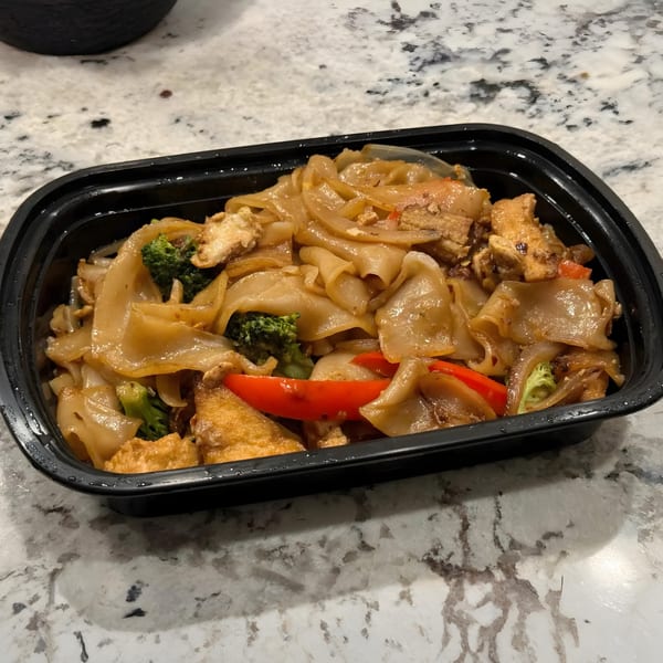 Noodle 501's Pad See Ew with wide noodles, tofu, broccoli, and red bell peppers in a black container.
