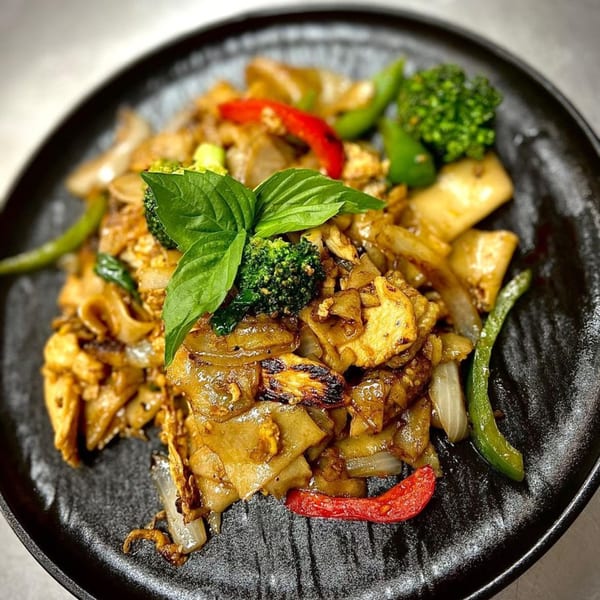 Noodle 501's Pad See Ew with wide noodles, chicken, broccoli, red peppers, and basil on a black plate.